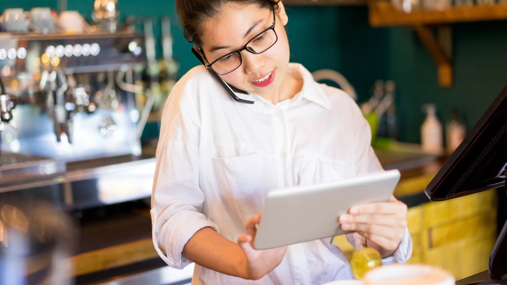 Photo of female restaurant staff member on phone and using a tablet 