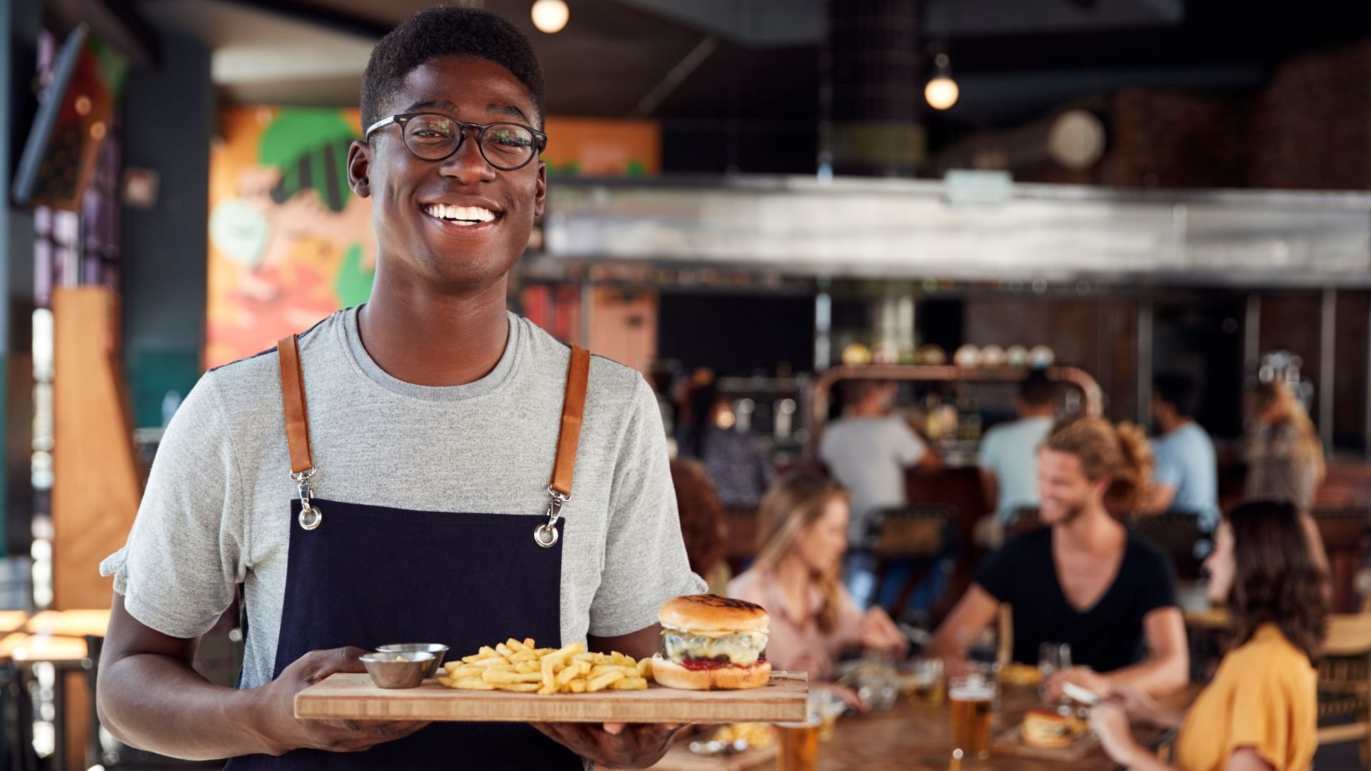Photo of male restaurant server holding a meal of burger and fries on a board in a gastro pub